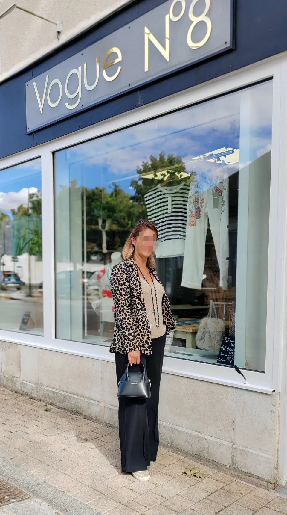 Femme portant veste léopard, pantalon noir, sac à main, devant vitrine de prêt-à-porter femme