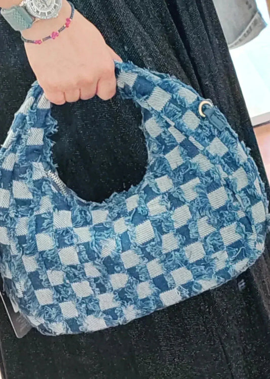 Sac à main denim imprimé petits carrés porté par une main, style moderne et tendance pour un look casual chic.