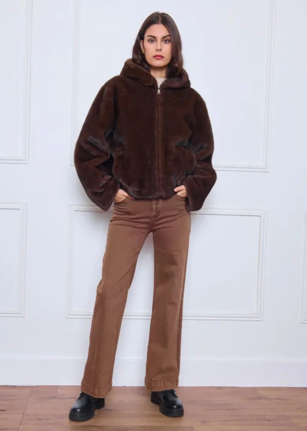 Femme portant une veste en fausse fourrure marron avec capuche et pantalon droit camel, look tendance automne-hiver.