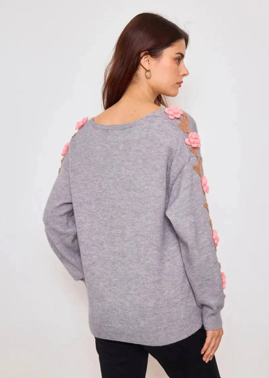 Femme portant un pull gris avec fleurs roses en relief sur les manches, vue de dos