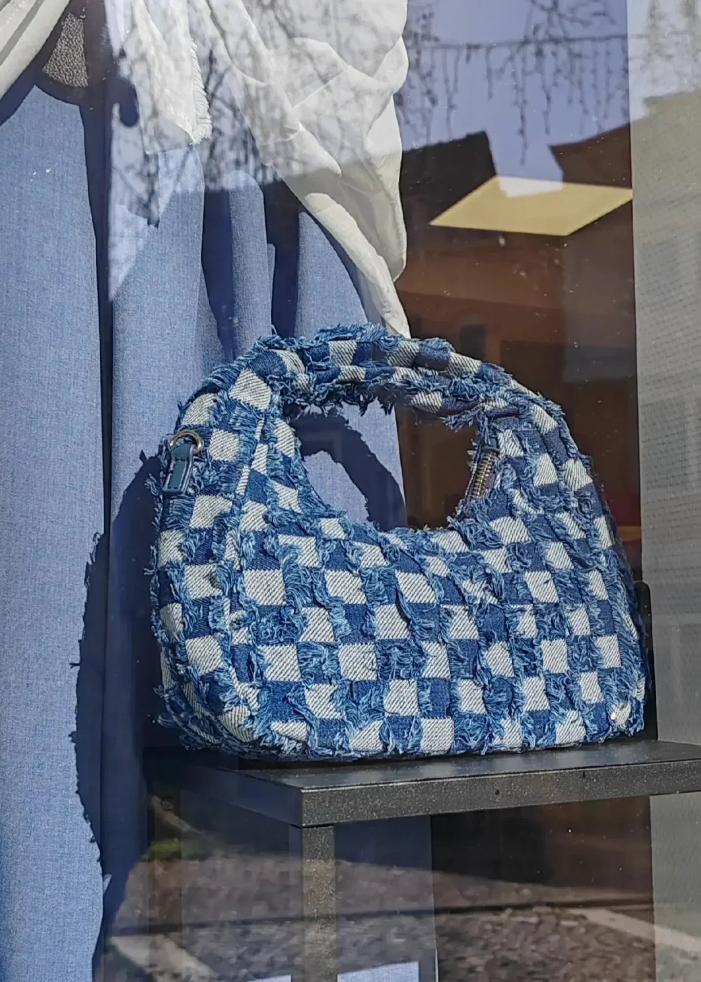 Sac à main denim imprimé petits carrés exposé dans une vitrine, style tendance et chic.